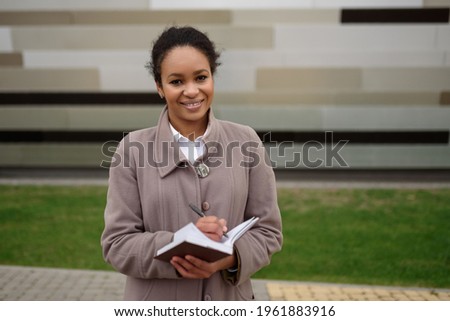 A businesslike African-American businesswoman makes a note in a notebook.