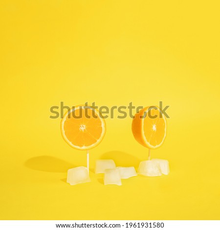 oranges on a sticks with yellow bright background with ice cubes.summer colorful idea