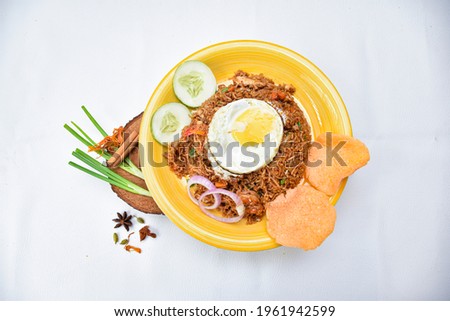  Nasi goreng fried rice with shrimps and egg garnished with fresh cucumber slices and prawn crackers on a yellow plate on white background. Asian food.
