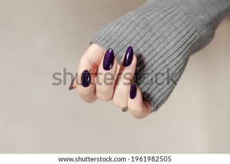 Female hand with long nails and dark purple lilac manicure holds a bottle of nail polish
