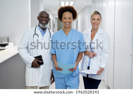Portrait of three diverse male and female doctors standing in hospital corridor smiling to camera. medicine, health and healthcare services.