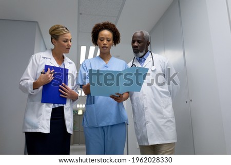 Three diverse male and female doctors standing in hospital corridor looking at medical documentation. medicine, health and healthcare services.