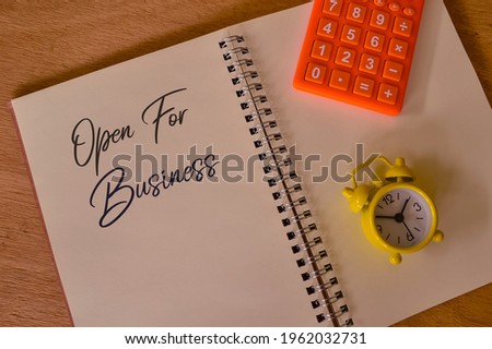 Phrase OPEN FOR BUSINESS written on notebook with clock and calculator.