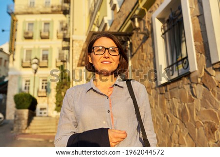Mature successful business woman walking along city street.