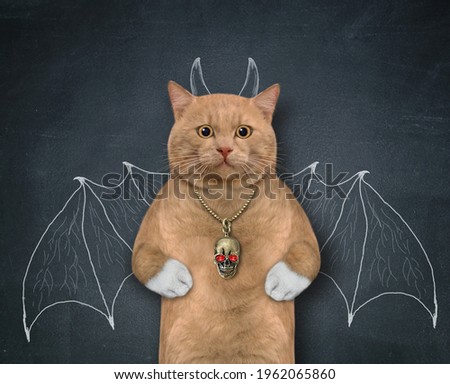 A reddish cat stands by a blackboard with bat wings and horns painted on it.