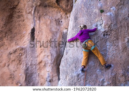 A girl trains strength and endurance on rocks, climbing on natural terrain, a rock climber overcomes a difficult route, an active lifestyle. rock climbing