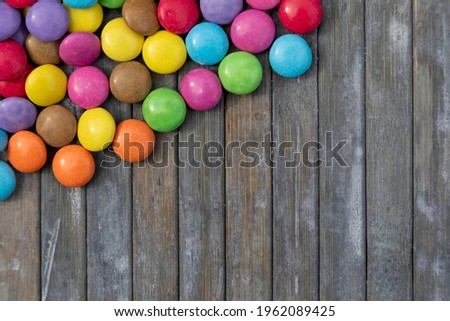 A grey wooden background with colourful round candies in the corner 
