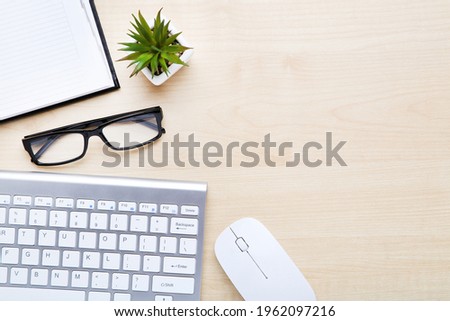 Computer keyboard with mouse, glasses and notepad on wooden table