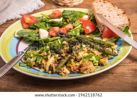 Fried scrambled eggs with asparagus, spinach and tomatoes in a large plate on a rustic wooden table, top view, close-up - simple rustic breakfast