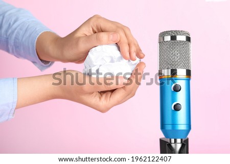Woman making ASMR sounds with microphone and crumpled paper on pink background, closeup