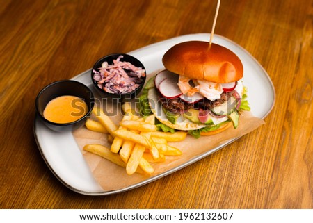 Whole picture of a burger with shrimps on a white plate, there are some french fries on it either. All on a wooden table.
