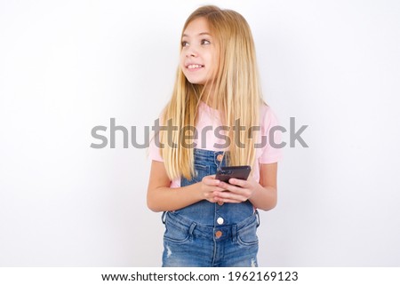 beautiful caucasian little girl wearing jeans overall over white background holding in hands showing new cell