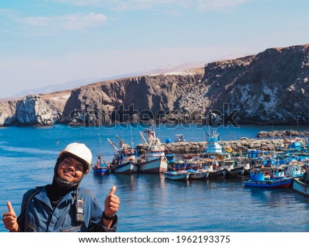 A Portrait photo of a man in boiler suit and safety helmet with fishing boat and sea background