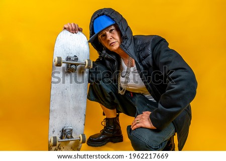 Funny portrait of mature woman. Lady having fun with skate dressed as rapper. Mature woman on colored backgrounds 
