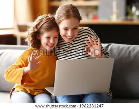 Happy family young loving mother and cute little girl daughter looking at computer screen, smiling and waving while having video call with family on laptop, relaxing together on sofa at home