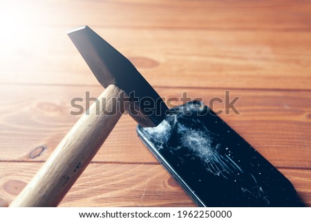 broken smartphone screen and hammer on wooden background