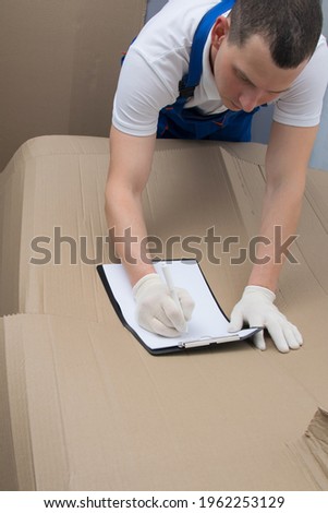 against the background of a large cardboard box, a loader in protective gloves fills out the documents for the goods