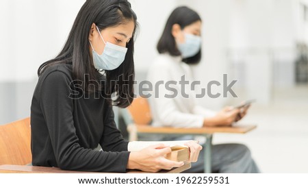 Female teenager college students wearing a face mask and keep distance while studying in classroom and college campus to prevent COVID-19 pandemic. Education stock photo