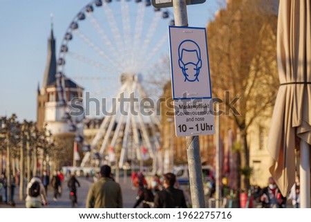 Selective focus at protective face mask signage on pole at promenade riverside of Rhine River in Düsseldorf, Germany to suggest people in wear mask during lockdown by epidemic COVID-19 during sunset. 