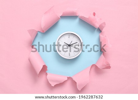 Clock through torn hole on blue-pink pastel background. Business concept. Pastel color trend. Minimalism