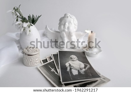 stack of vintage photos, baby photography of 1960, selective focus on photo, candle is lit, first spring flowers, snowdrop, Galanthus in vase, concept of family tree, genealogy, childhood memories
