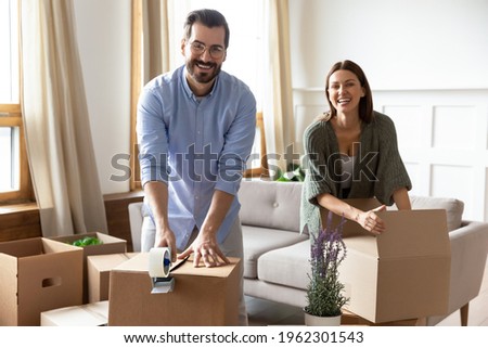 Portrait of smiling young Caucasian couple renters pack boxes packages relocate together. Happy man and woman tenants seal parcels moving to new home. Relocation, rental, rent concept. Royalty-Free Stock Photo #1962301543