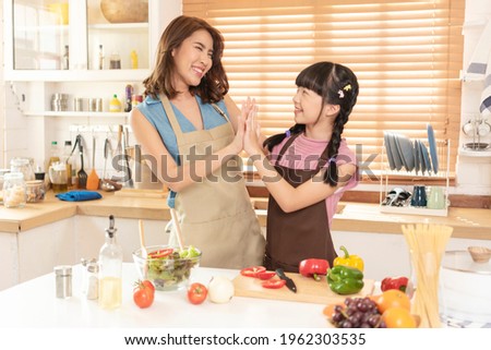 Asian family, mother and daughter enjoy cooking salad together in kitchen room at home.