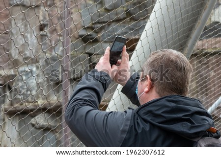 a man holds his hands up and takes pictures on his phone at the zoo