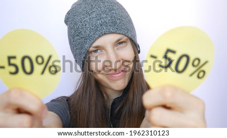 A cute girl dressed in street style shows two yellow round signs with -50 percent discount close-up