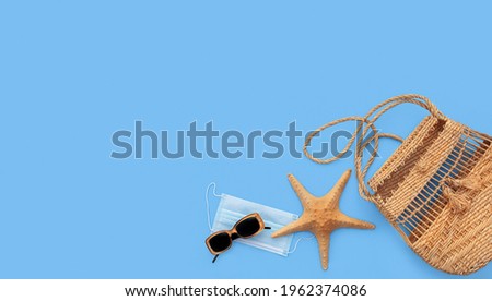 Summer blue background with a protection coronavirus mask, beach bag, a starfish, sunglasses and with copy space.