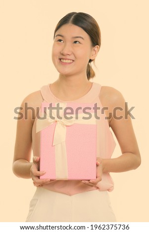 Thoughtful young happy Asian woman smiling and holding gift box
