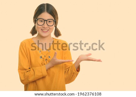 Studio shot of young happy Asian woman smiling while showing something