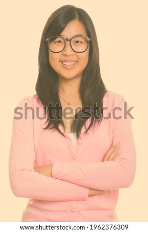 Portrait of happy young beautiful Asian nerd woman smiling with arms crossed