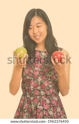 Young happy Asian woman choosing between green and red apple