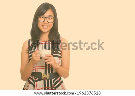 Portrait of happy young beautiful Asian businesswoman with coffee cup