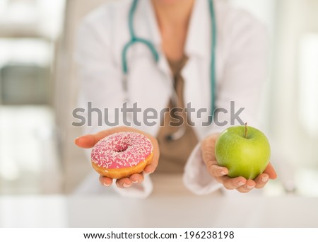 Closeup on medical doctor woman giving a choice between apple and donut Royalty-Free Stock Photo #196238198