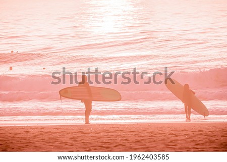 Pink Ocean Landscape in Sunset Time Background with Sandy Beach and Wavy Sea. Surfers stand on the beach with surfboard at colorful sunset. Defocused photo with soft focus and blur in motion. 