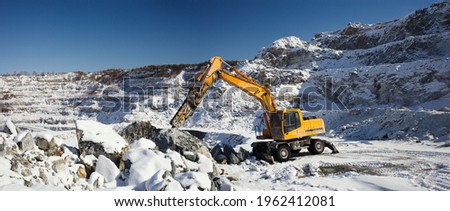 Quarry machine hydraulic breaker works in a winter stone quarry, panorama.