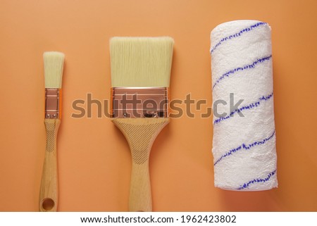 two construction brushes of different widths and a roller lie on an orange background. photo taken close-up from above