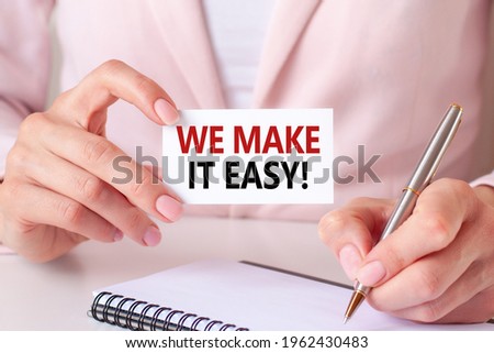 Woman writes in a notebook with a silver pen and hand holding card with text: we make it easy. Pink background, front view. Business and education concept.