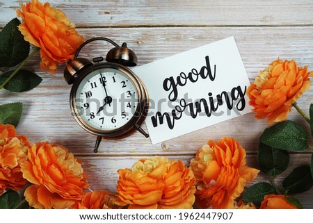 Good Morning card and alarm clock with orange flower decoration on wooden background