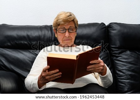 Lady with glasses reading a book on the sofa at home