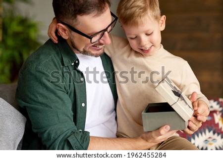 Portrait of young loving father wearing eyeglasses giving his happy cute son birthday or christmas present, wrapped gift box with bow, selective focus. Family holidays and celebration concept