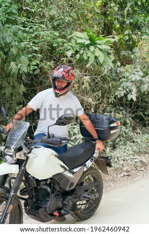 Hispanic Man next to his motorcycle on a rural road