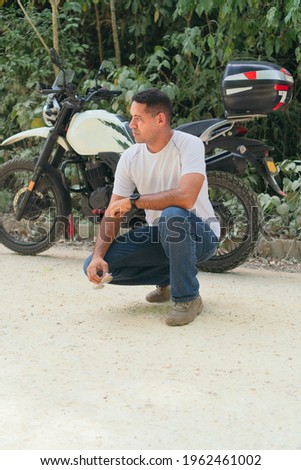 Serious young ethnic biker in casual clothes near motorcycle