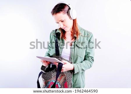 Self-confident beautiful young woman on white background wearing casual clothes and headphones looking at the tablet from work