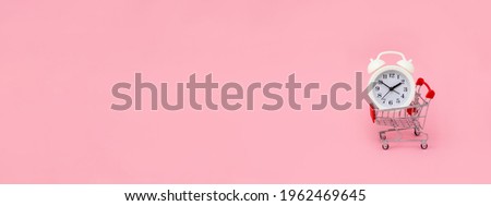 White alarm clock and shopping cart on pink background. Sale time concept. Horizontal banner. Copy space.