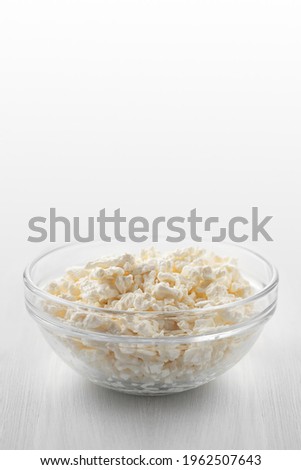 Fresh homemade farm cottage cheese in a glass bowl on a white wooden table. Vertical image