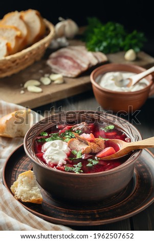 Freshly cooked borscht - traditional dish of Russian and Ukrainian cuisine in earthenware dish with bacon, sour cream and garlic, vertical image