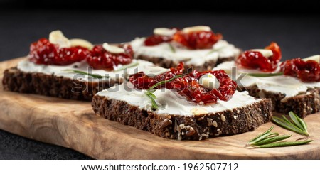 Homemade multigrain bread sandwiches with cream cheese and sun-dried tomatoes on a wooden platter. Healthy eating concept